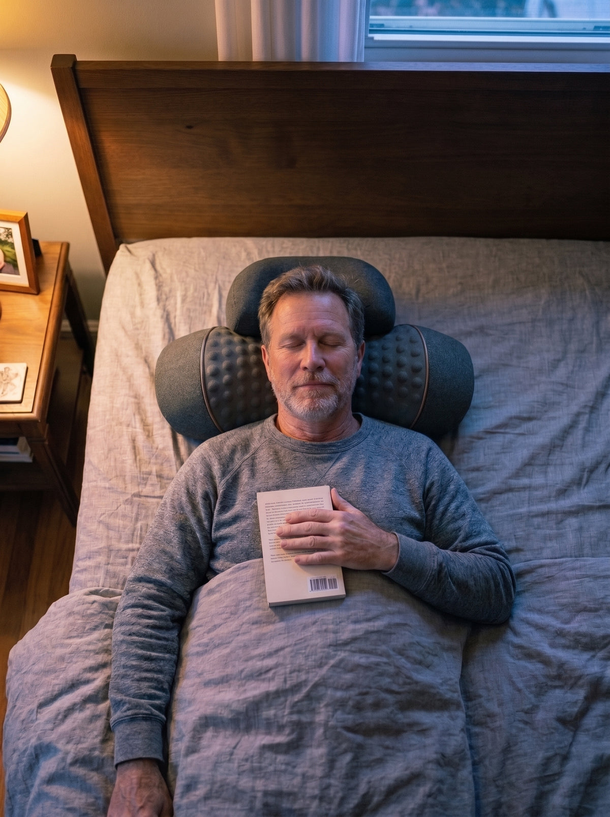 A man lying in bed with his head on the Napewell pillow, reading lamp on